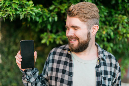 Happy bearded man showing blank smartphone screen over green leaves background - empty space for advertising and copy spaceの写真素材