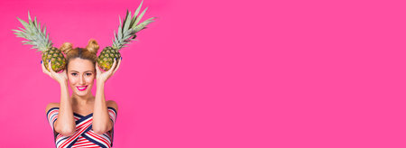 Fashion portrait funny woman with pineapple banner over pink background with copy space and place for advertisingの写真素材