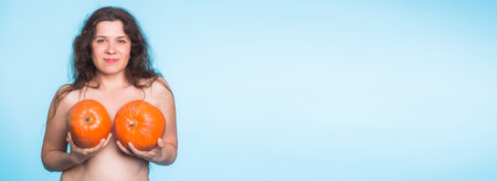 Breasts implant banner concept - Happy woman holding two pumpkins in front of her breasts on blue background with copy space and place for advertisingの写真素材