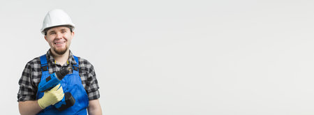 Happy caucasian male builder worker with screwdriver on white background banner with copy space, wearing white helmet.の写真素材