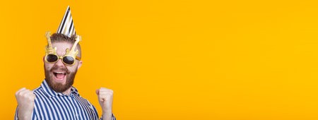 Crazy young positive hipster guy with a beard laughs happily on a yellow background banner with copy...