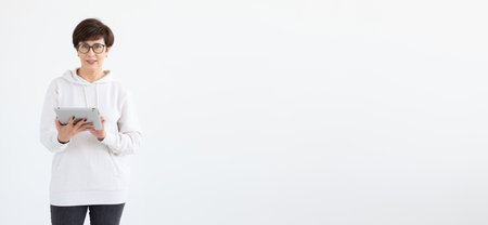 Beautiful woman 50 years old with short hair holding tablet on white banner background with copy space and place for advertisingの写真素材