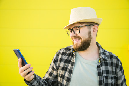 Portrait of attractive cheerful guy using smartphone for scrolling on social media over bright vivid...