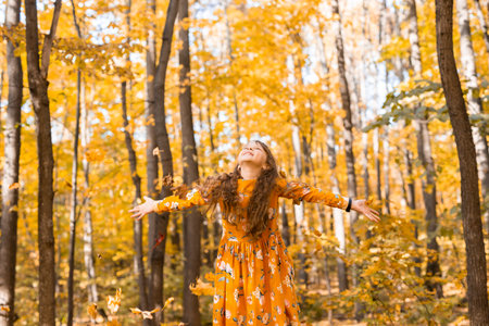 Child girl throwing fall leaves on autumn nature - fun, leisure and childhood concept