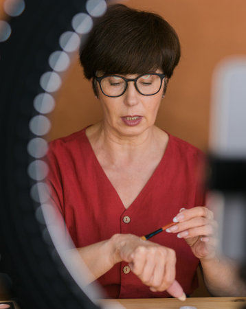Beauty and cosmetics e-commerce and blogging concept - professional mature female make up artist testing new cosmetics recording video review on cosmetic products at homeの写真素材