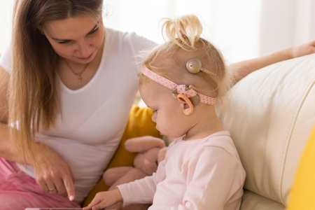 Child girl with cochlear implant with her mother at home. Hear impairment and deaf community and diversity conceptの写真素材