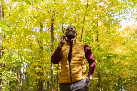 Portrait of smiling african american man talking on mobile phone outside in autumn park - business communication and technologies conceptの写真素材