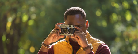 Banner african american guy photographer taking picture with vintage camera on city green park -...