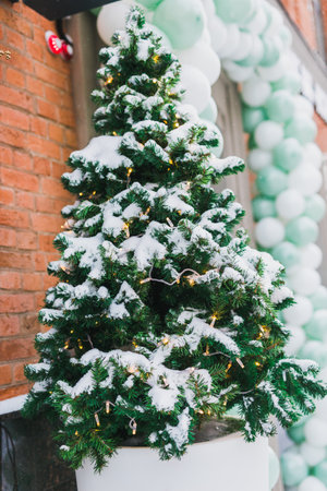 Stylish decorated christmas tree outdoor near store window with snow. Winter holidays and decor for xmasの写真素材