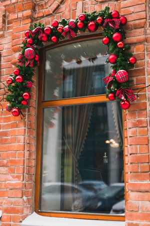 Stylish christmas fir branches with red baubles and sparkling garland on front of window at holiday market or restaurant in city street. Winter christmas street decorの写真素材
