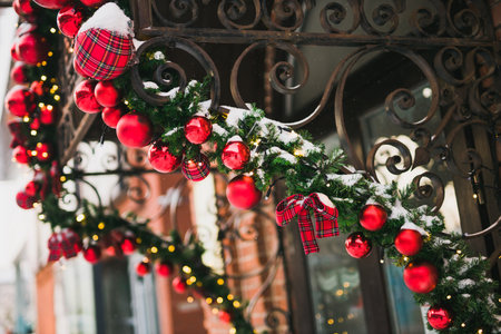 Stylish christmas fir branches with red baubles and sparkling garland on front of door at holiday market or restaurant in city street. Winter christmas street decorの写真素材
