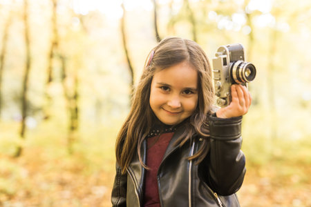 Little girl with photo with old retro camera in autumn nature. Leisure and hobby concept.の写真素材
