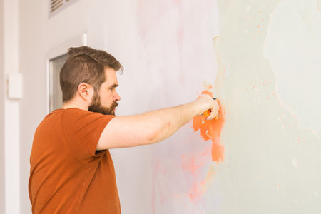 Man smoothes wall surface with a wall grinder. Male grind a white plaster wall - renovation and redecoration conceptの写真素材