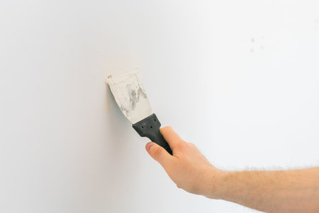 Close Up view of a mans hand plastering hole in a wall with spatulaの写真素材