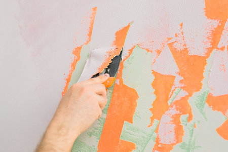 Close up man smoothes wall surface with a wall grinder. Male grind a white plaster wall - renovation and redecoration concept. Copy space and empty space for textの写真素材