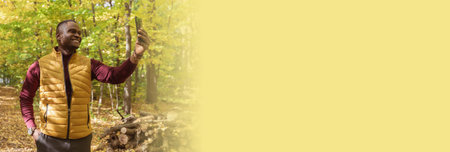 Banner African American man taking a self portrait with a smartphone in autumn fall park copy space and empty space for text. Happy people, season and new normality conceptの写真素材