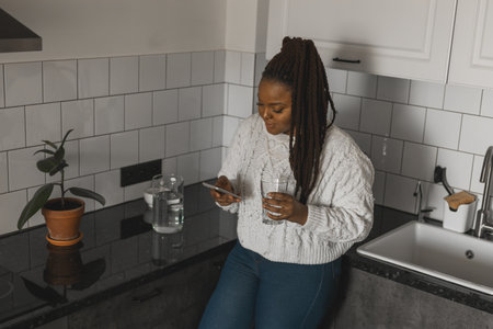 Portrait of good-looking African female student dressed casually holding mobile phone and typing messages and communicating with friends social networks using high-Internet connection.の写真素材
