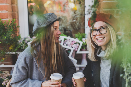 Young female best friends talking to each other discussing interesting themes during free time hipster girls, joking and having fun together enjoying recreation with coffee to go on urbanの写真素材