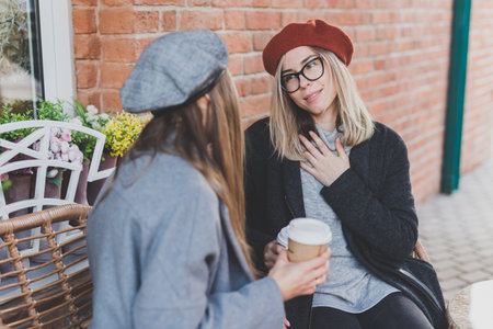 Young female best friends talking to each other discussing interesting themes during free time hipster girls, joking and having fun together enjoying recreation with coffee to go on urbanの写真素材