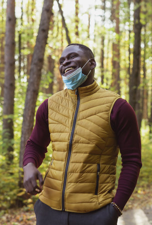 Handsome african american man wearing casual clothes and medical mask smiling happy walking in city park - end of pandemicの写真素材