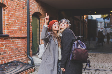 Two girls walking on street together and holding their hands. They are wearing spring or autumn clothes and they are happy. Friendship and relationship conceptの写真素材