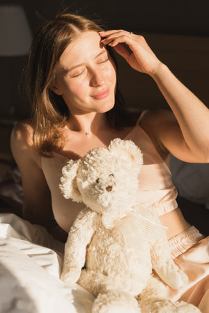 Portrait girl is waking up in morning stretches in bed and sun shines from the window. Happy young woman greets new sunny dayの写真素材