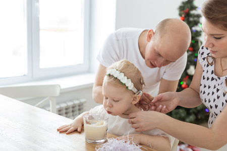 Mother and father helps to put on cochlear implant for their deaf baby daughter in christmas living room. Hearing aid and innovating medical technologies treatment deafnessの写真素材