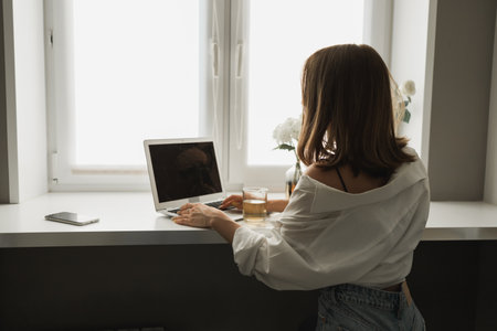 Close up of back view young pretty concentrated woman typing and browsing online on laptop working on computer while sitting in cozy room alone. Distance learning and work conceptの写真素材