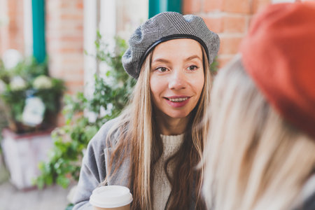 Young female best friends talking to each other discussing interesting themes during free time hipster girls, joking and having fun together enjoying recreation with coffee to go on urbanの写真素材