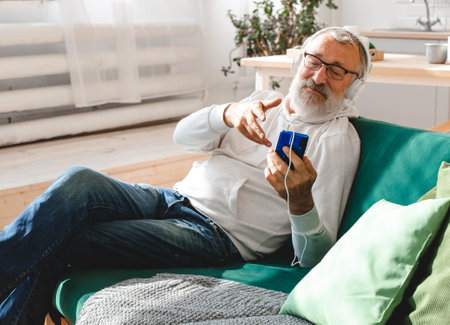 Elderly man cool bearded old man using mobile phone for video call - happiness elderly lifestyle people concept. Video call on smartphone in room waving to screen and chatting with children - modern technologies communication and internet.の写真素材