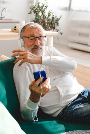 Elderly man cool bearded old man using mobile phone for video call - happiness elderly lifestyle people concept. Video call on smartphone in room waving to screen and chatting with children - modern technologies communication and internet.の写真素材