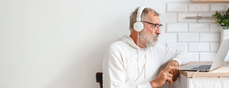 Banner handsome old man dressed in hoodie and eyeglasses is using laptop and smiling while listen music sitting on couch at home copy space and empty place for textの写真素材