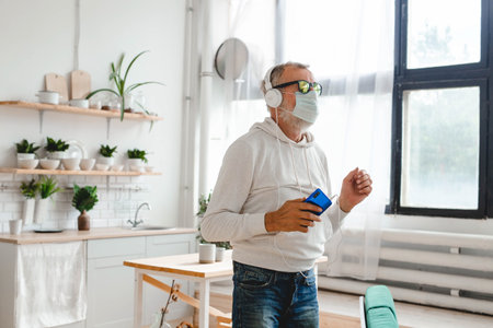 Senior man with medical mask on face using smartphone app for creating playlist music - Elderly male having fun with mobile phone technologyの写真素材
