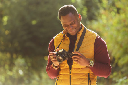 African american guy photographer taking picture with vintage camera on city green park - leisure...