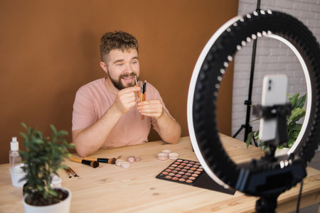 Man talking on cosmetics holding a makeup tools while recording his video. Guy making video for his blog on cosmetic productの写真素材