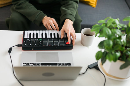 Top view of music producer or arranger using laptop and midi keyboard and other audio equipment to...