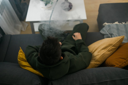 Bearded man is smoking hookah at home and blowing cloud of smoke - chill time and resting conceptの写真素材