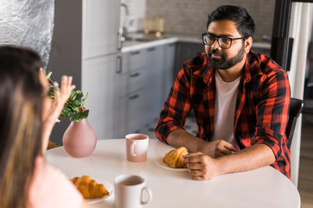 Happy indian couple having breakfast and small talk together in the kitchen - friendship, dating and familyの写真素材