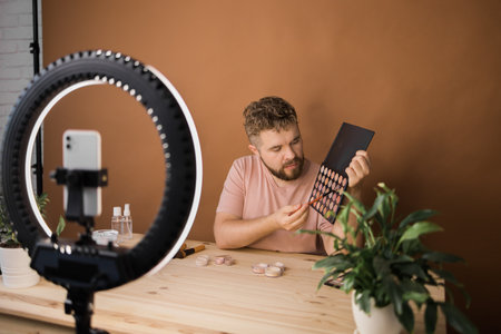 Man vlogging about make up and beauty products. Male shooting a makeup tutorial. Guy teaching make up tutorial using her phone - diversity and blogger concept.の写真素材