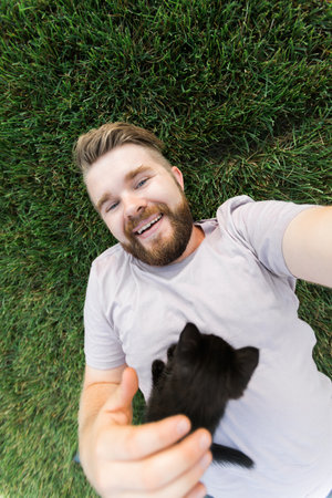 Man with little kitten lying and playing on grass - friendship love animals and pet owner conceptの写真素材