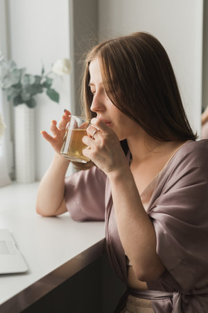 Young woman sitting on chair at home and drinking tea, casual style indoor shoot. Close-up portrait
