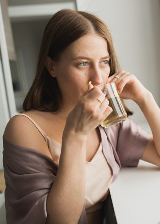Young woman sitting on chair at home and drinking tea, casual style indoor shoot. Close-up portraitの写真素材