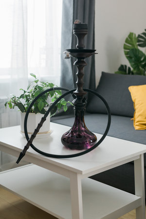 Hookah shisha with glass flask and metal bowl in room background. Traditional Eastern vacation for...