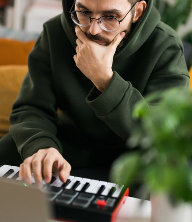 Recording electronic music track with portable midi keyboard on laptop computer in home studio. Producing and mixing music, beat making and arranging audio content with professional audio devicesの写真素材