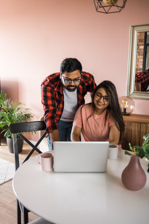 technology remote job and lifestyle concept - happy indian man and woman in glasses with laptop computer working at home officeの写真素材