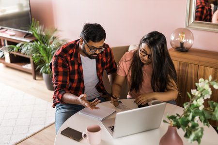 Serious wife and husband planning budget, checking finances, focused young woman using online calculator, counting bills or taxes, man using laptop, online banking services. Family sitting at table in kitchen - economic crisis conceptの写真素材
