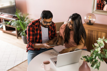 Serious wife and husband planning budget, checking finances, focused young woman using online calculator, counting bills or taxes, man using laptop, online banking services. Family sitting at table in kitchen - economic crisis conceptの写真素材
