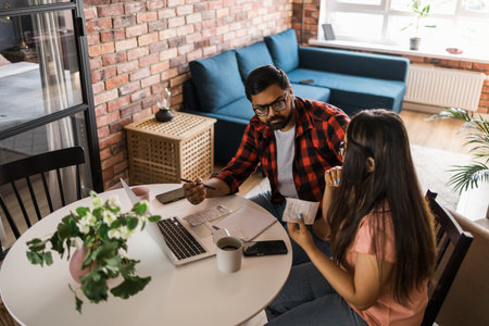 Serious wife and husband planning budget, checking finances, focused young woman using online calculator, counting bills or taxes, man using laptop, online banking services. Family sitting at table in kitchen - economic crisis conceptの写真素材
