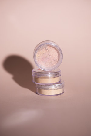 Mineral powder for skin tone color in small containers on pale rose colour background with shadows -...