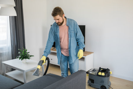Man in protective rubber glove cleaning sofa with professionally extraction method with washing vacuum cleaner. Early spring regular cleanup. Commercial cleaning company conceptの写真素材